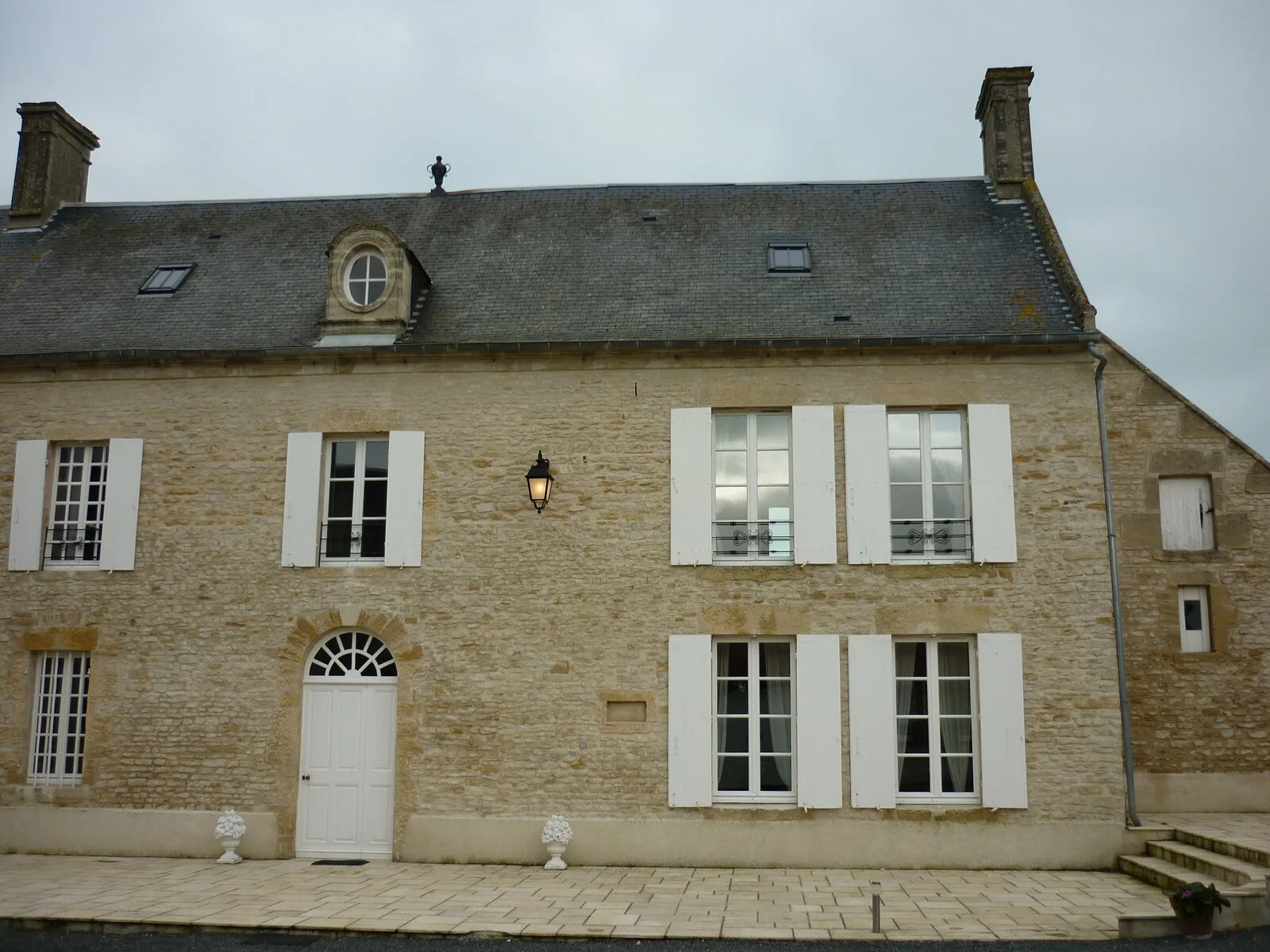 Gîte de groupe Logis du Pavillon à Longues-sur-Mer — Façade en pierre normande du logis avec volets blancs, lucarnes en pierre et grande cour pavée, capacité 15 personnes