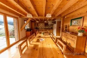 Cuisine et salle à manger en bois avec longue table dressée pour un groupe, vue sur la campagne