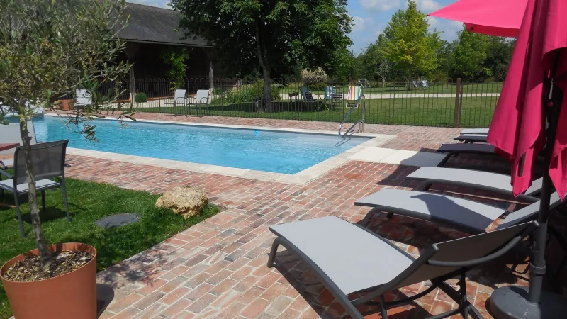 Piscine extérieure entourée d'une terrasse en briques avec transats et parasol