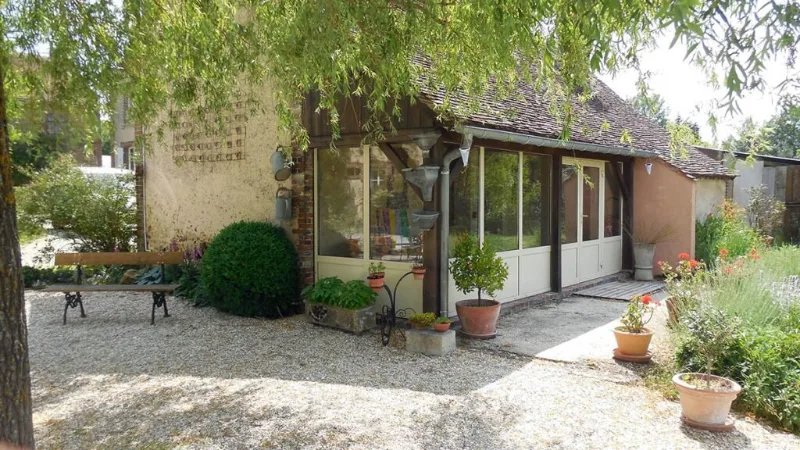 Véranda et bâtiment annexe du domaine entourés d'un jardin arboré et fleuri
