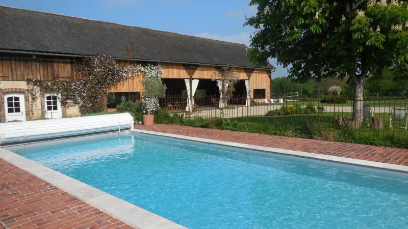Façade en pierre et bois du domaine avec grande piscine chauffée au premier plan
