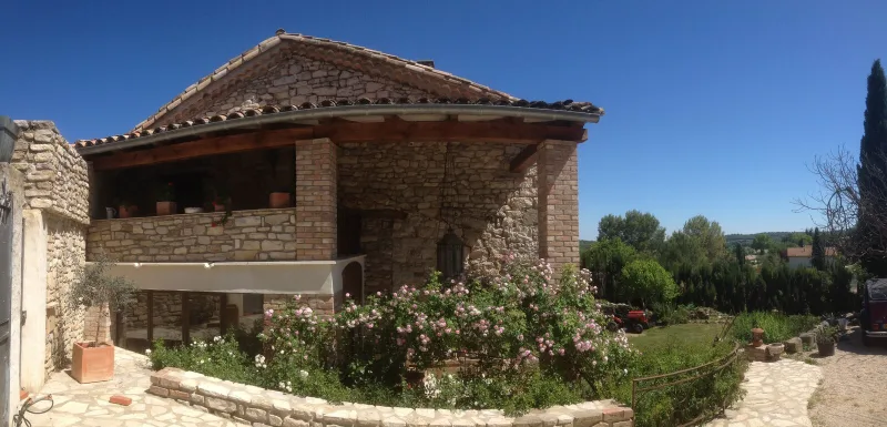 Façade en pierre du mas avec toiture provençale, roseraie et vue sur la campagne