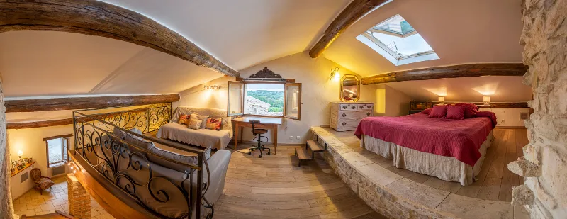 Chambre mansardée avec lit double, poutres apparentes et fenêtre ouverte sur le village