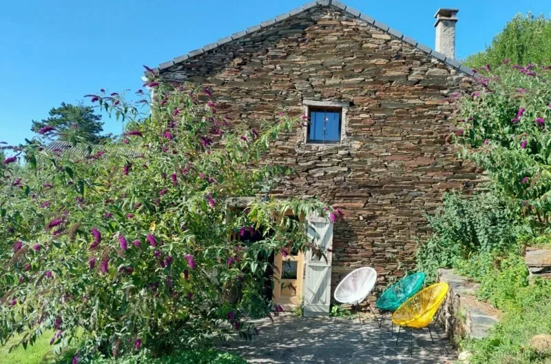 Pignon en pierre du gîte orné de buddleias fleuris avec chaises colorées à l'entrée