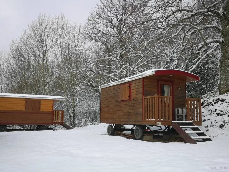 Roulottes en bois sous la neige avec terrasses et escaliers d'accès, nichées dans la forêt