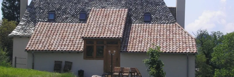 Façade en pierre du gîte avec toiture de lauzes, lucarnes et terrasse extérieure