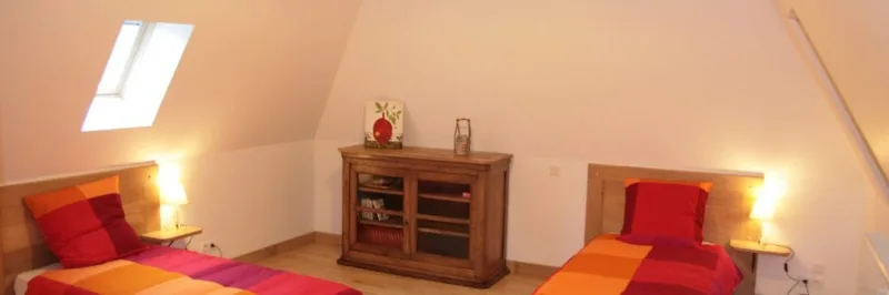 Chambre mansardée avec deux lits simples colorés et fenêtre de toit lumineuse