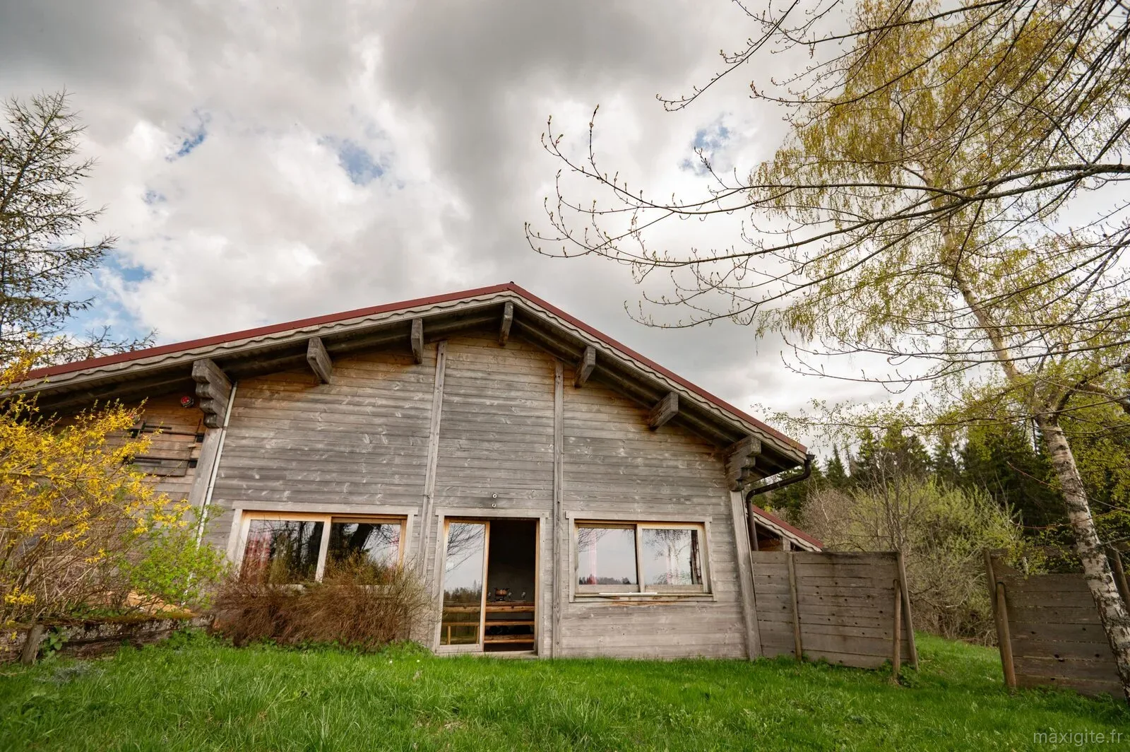 Gîte de groupe La Pourvoirie - Refuge Sous La Joux à Les Moussières — Facade en bois du chalet en lisiere de foret avec grand jardin, capacité 12 personnes