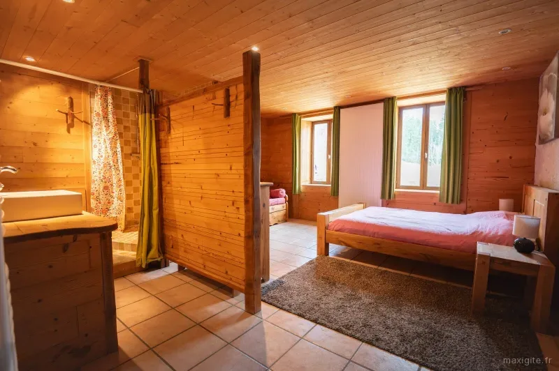 Chambre avec salle d'eau ouverte, murs en bois et lit double
