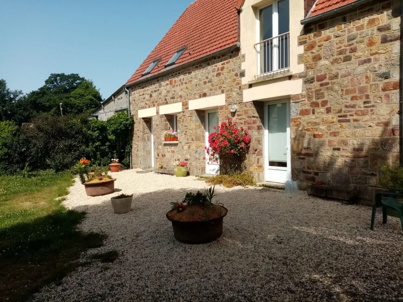 Facade en pierre du corps de ferme normand avec terrasse gravillonnee et rosier fleuri