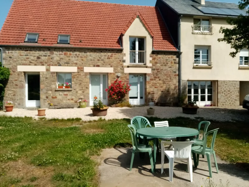 Jardin avec table et chaises de jardin devant la facade en pierre du gite