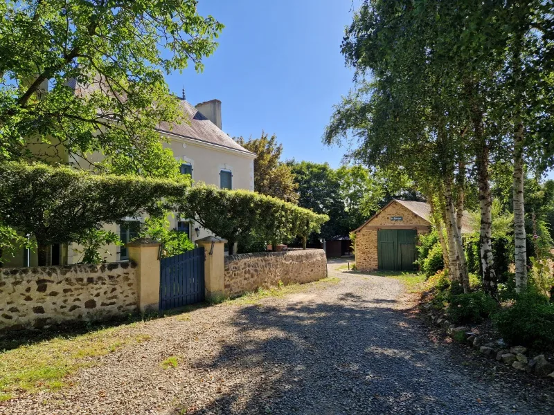 Facade en pierre du domaine avec allee gravillonnee et dependance en pierre