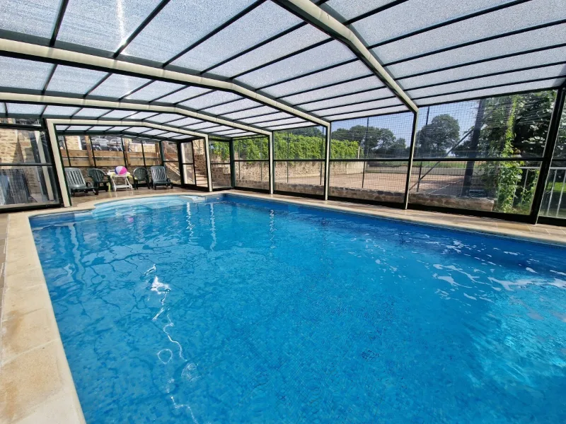 Piscine interieure chauffee sous verriere avec transats et vue sur le court de tennis