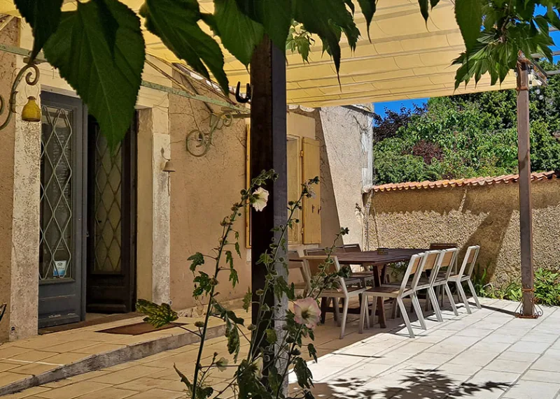 Terrasse couverte avec table dressee et vue sur la facade en pierre du gite
