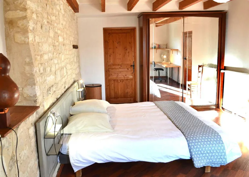 Chambre avec mur en pierre apparente, lit double et armoire miroir