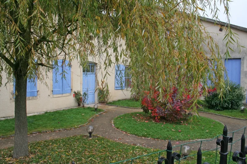 Façade du gîte avec volets bleus et jardin arboré dans le village