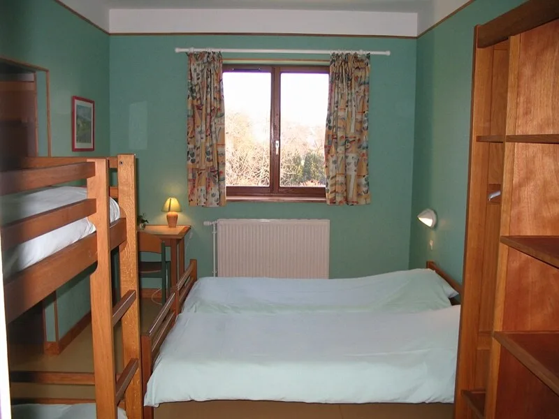Chambre avec lits superposés et lit simple, murs verts et vue sur les arbres