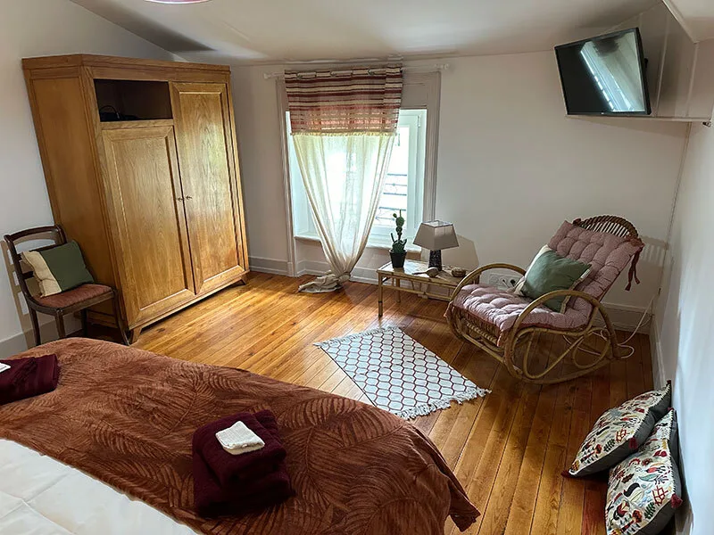 Chambre avec parure bordeaux, fauteuil en rotin et parquet en bois clair