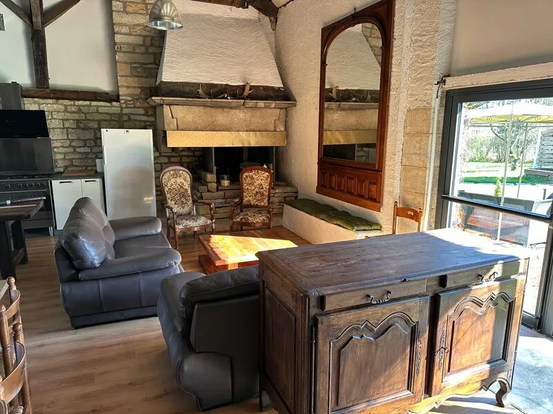 Salon avec cheminée en pierre, fauteuils anciens et grande baie vitrée