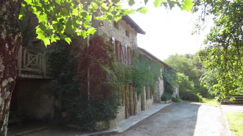 Façade en pierre du corps de ferme couverte de vigne vierge, avec balcon en bois