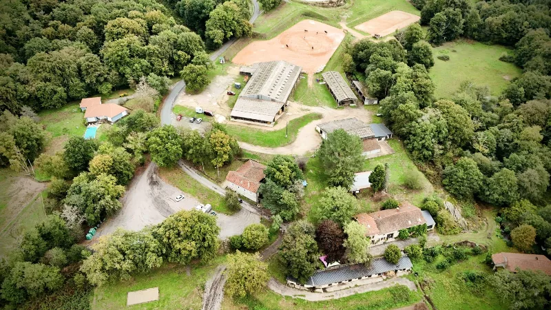 Vue aérienne du domaine équestre avec manège, bâtiments et gîtes entourés d'arbres