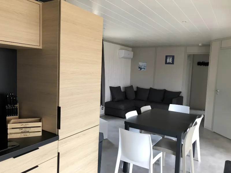 Salon avec canapé d'angle sombre et coin repas donnant sur la cuisine ouverte