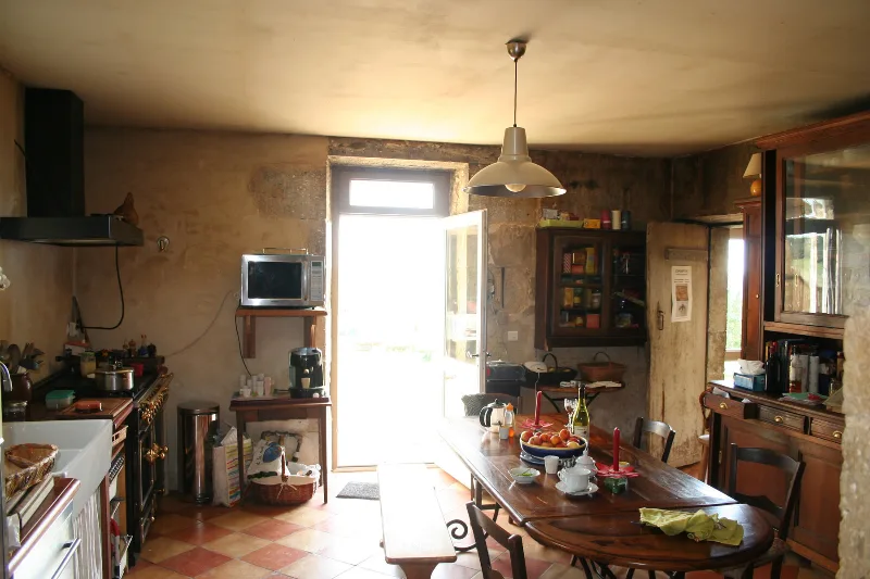Cuisine traditionnelle avec grande table en bois, cuisinière et porte donnant sur le jardin
