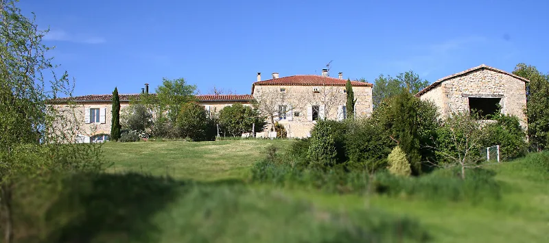 Vue d'ensemble des bâtiments du domaine en pierre blonde entourés de verdure