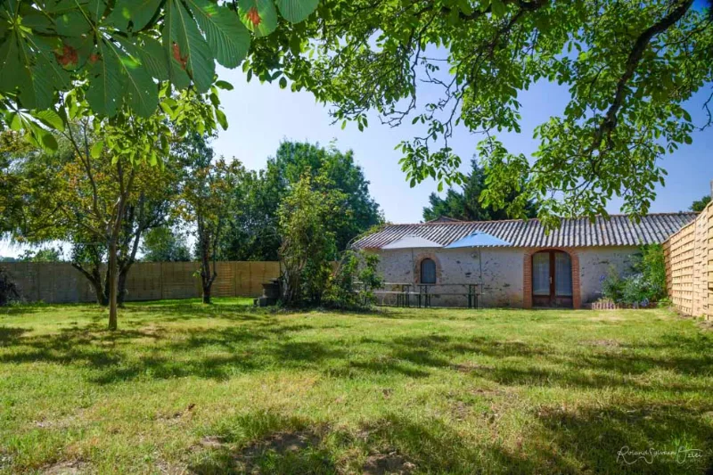 Grand jardin arboré et clos avec vue sur la toiture en tuiles du gîte et terrasse ombragée