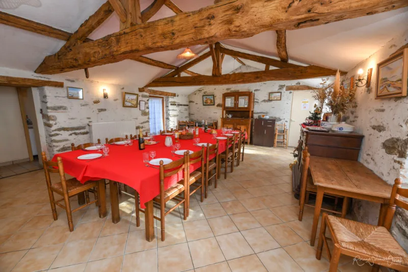 Grande salle de réception aux poutres apparentes avec longue table dressée en rouge pour tout le groupe