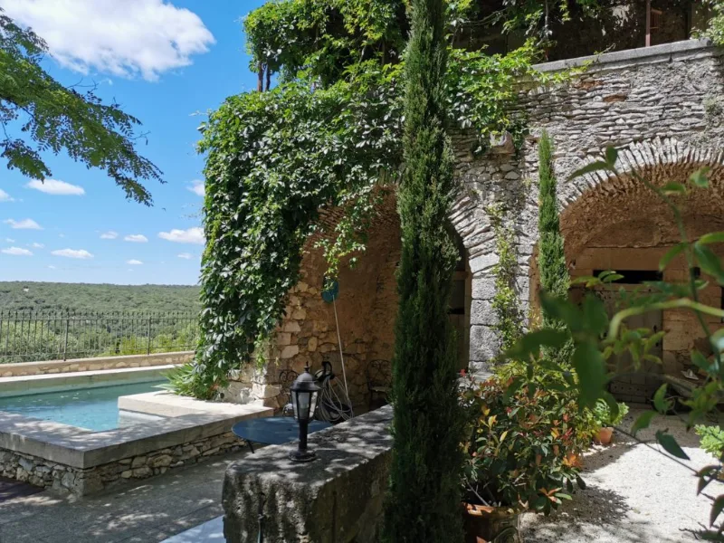 Piscine en pierre sur terrasse dominant la campagne, entourée de murs anciens couverts de vigne vierge