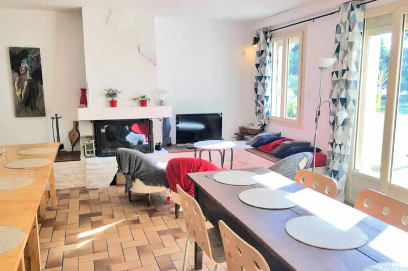 Grand séjour lumineux avec cheminée, tables dressées et baies vitrées donnant sur le jardin