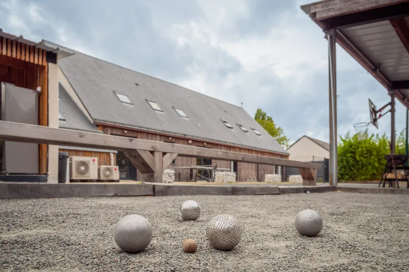 Terrain de pétanque extérieur avec boules et vue sur la maison et son panier de basket