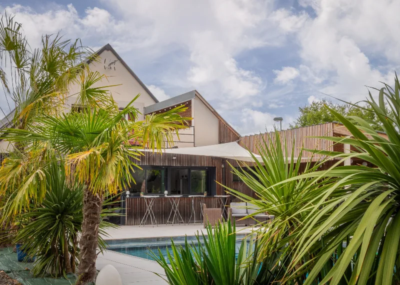 Piscine extérieure entourée de palmiers avec espace bar et coin salon ombragé