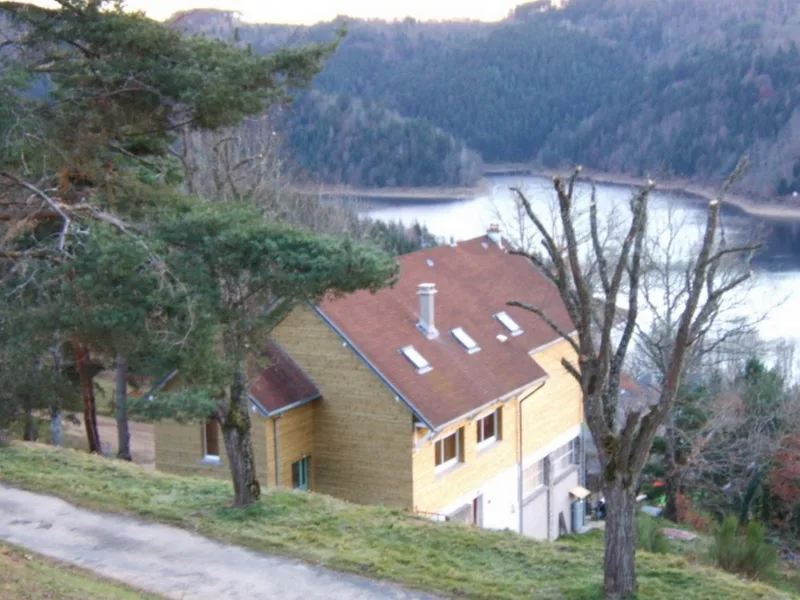 Maison en bois surplombant le lac de Garabit-Grandval entourée de forêt de pins