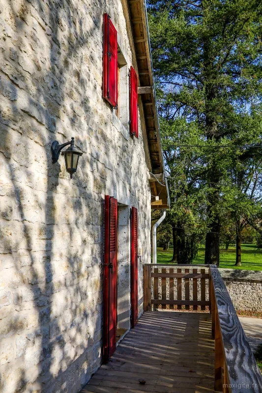 Détail de la façade en pierre calcaire avec volets rouges et terrasse en bois sur le parc