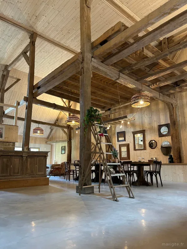 Grande grange aménagée avec charpente apparente, bar en bois et coin salon avec miroirs anciens