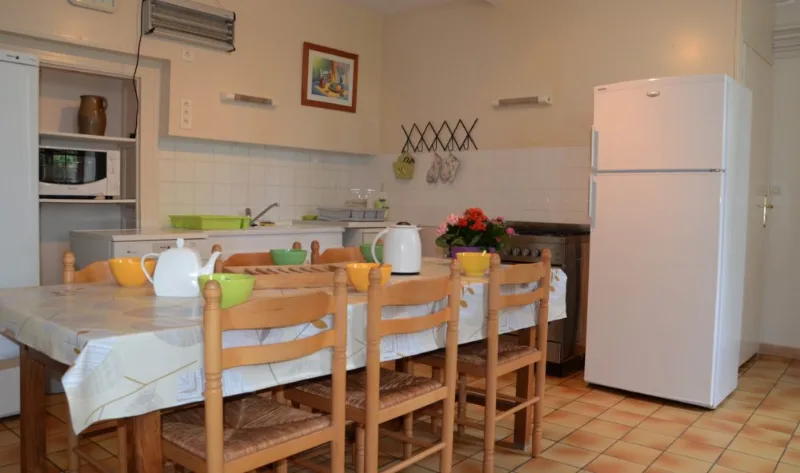 Cuisine collective avec grande table et chaises pour les repas, réfrigérateur et four professionnel