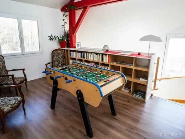 Salle de jeux sous charpente avec baby-foot, fauteuils et bibliothèque