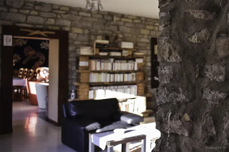Salon intérieur en pierre apparente avec bibliothèque et vue sur la salle à manger