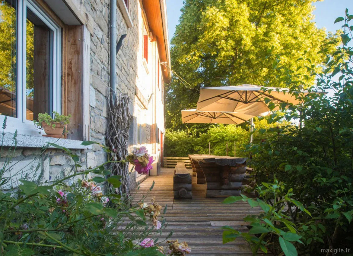 Gîte de groupe Les Terrasses de Merlue à Plaisia — Terrasse en bois ombragée devant la ferme en pierre avec grande table extérieure et parasols, capacité 26 personnes