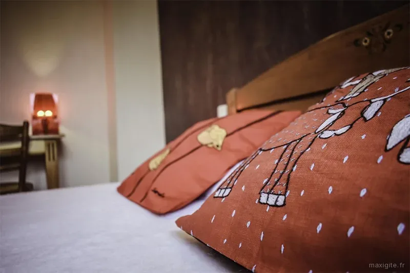 Chambre cosy avec lit et coussins imprimés orangés, éclairée par une lampe de chevet