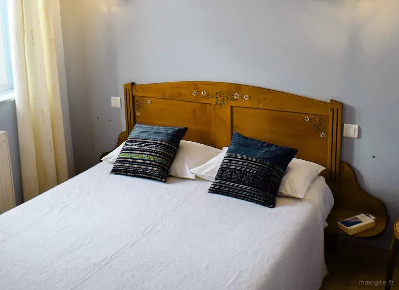 Chambre lumineuse avec grand lit, tête de lit en bois peint et coussins en tissu wax