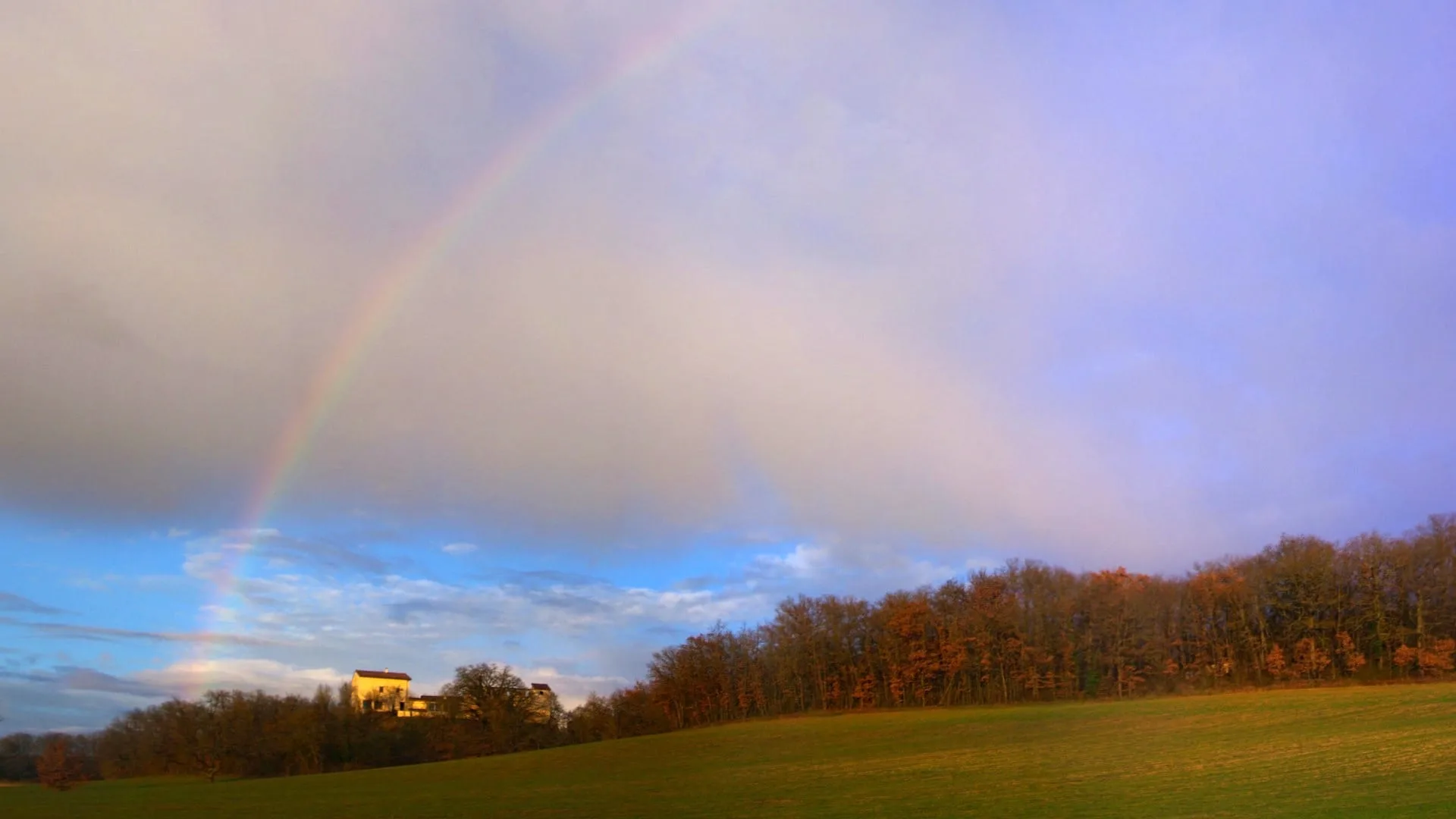 Vue d'ensemble du domaine sous un arc-en-ciel, entouré de bois et prairies