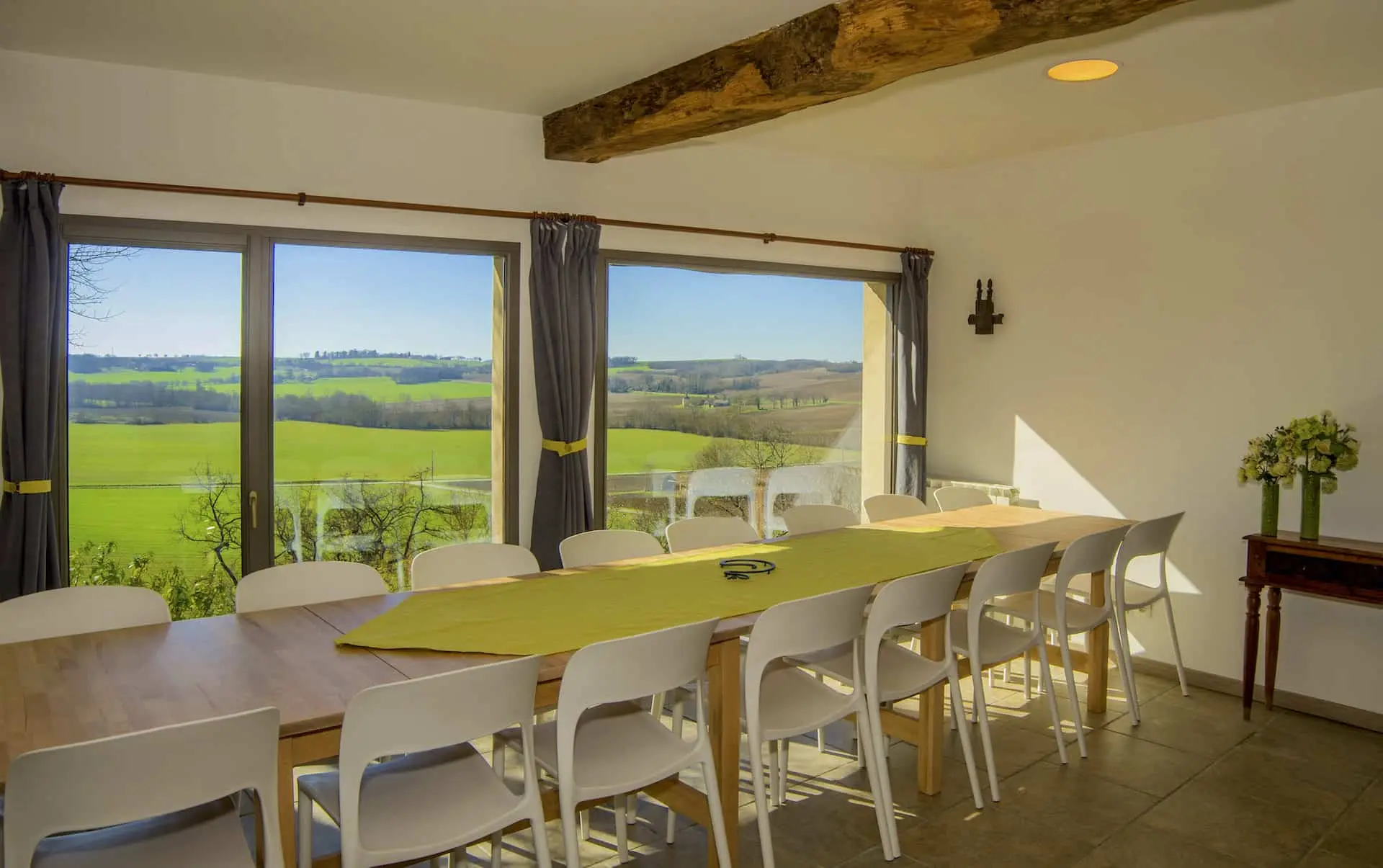 Grande salle à manger avec poutres apparentes et vue sur les coteaux gersois