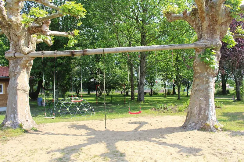 Aire de jeux extérieure avec balançoires et dôme d'escalade sous les arbres