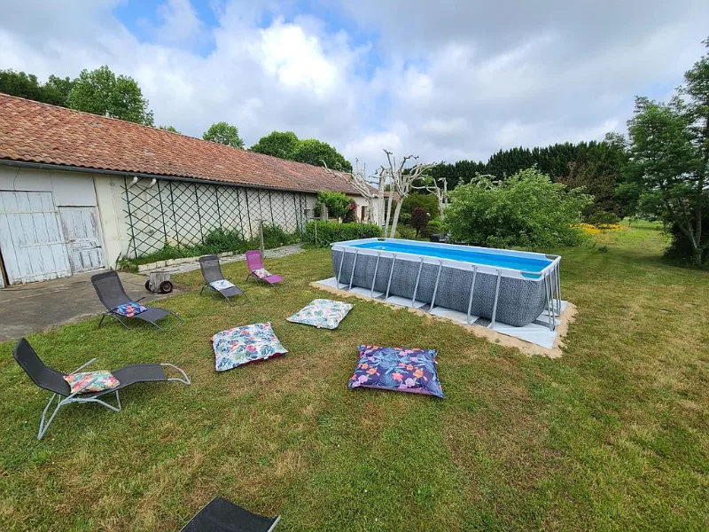 Piscine hors-sol entourée de transats devant l'ancienne grange en pierre