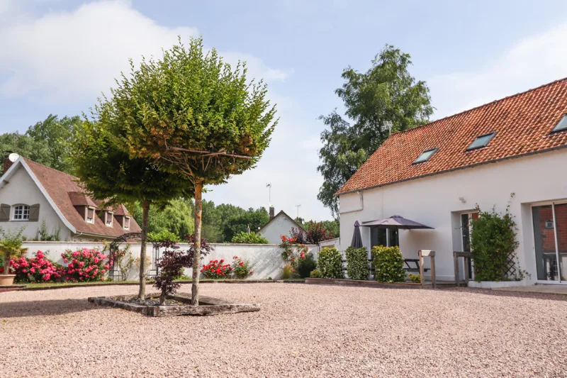 Cour gravillonnée entre les deux bâtiments du domaine, jardin fleuri et toits en tuiles