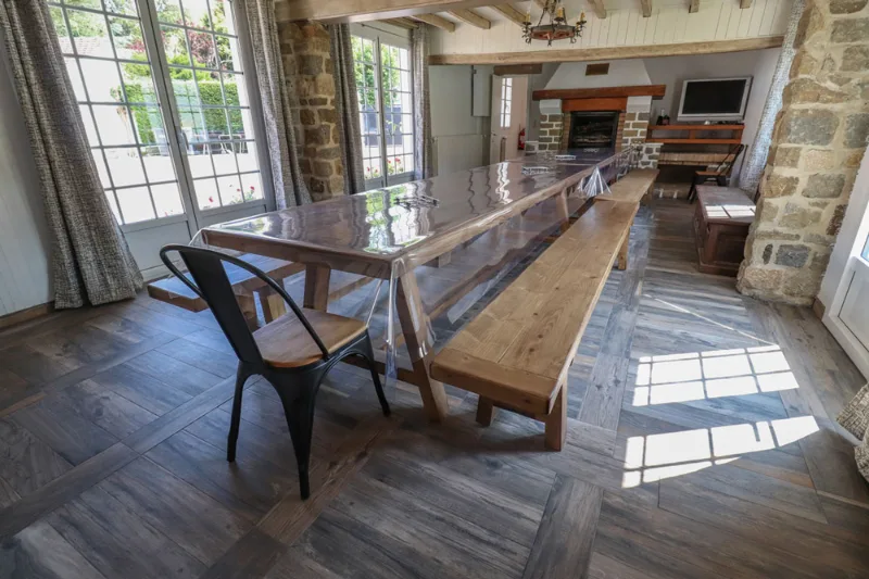 Grande salle à manger avec longue table en bois, cheminée en pierre et poutres apparentes