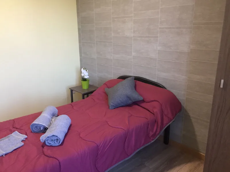 Chambre individuelle avec lit simple, mur en carrelage gris et lampe d'appoint